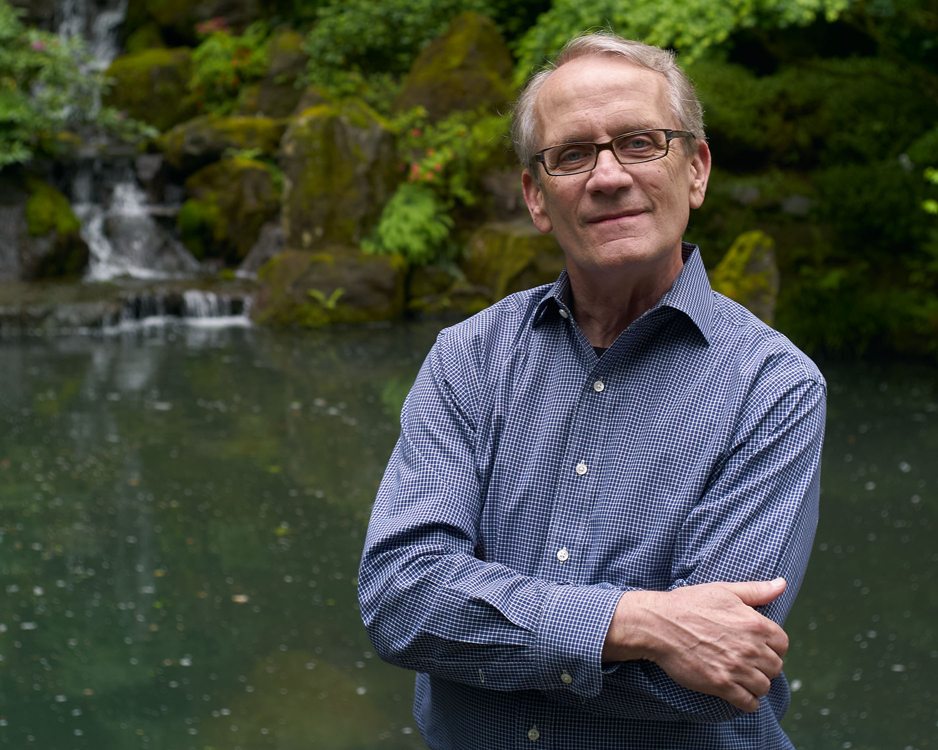 Environmental headshot of a man with arms crossed in front of a waterfall and lush greenery — Headshots by Guffy, San Diego