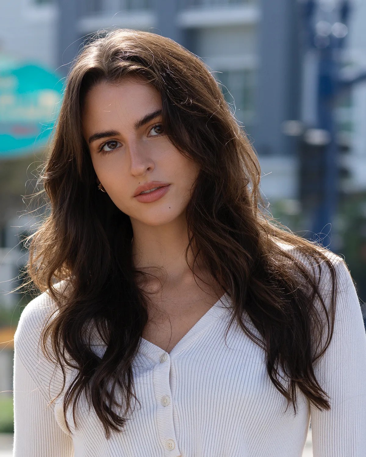 Actor and model headshot of a young woman with dark hair in a white ribbed cardigan, photographed outdoors on an urban street — Headshots by Guffy, San Diego