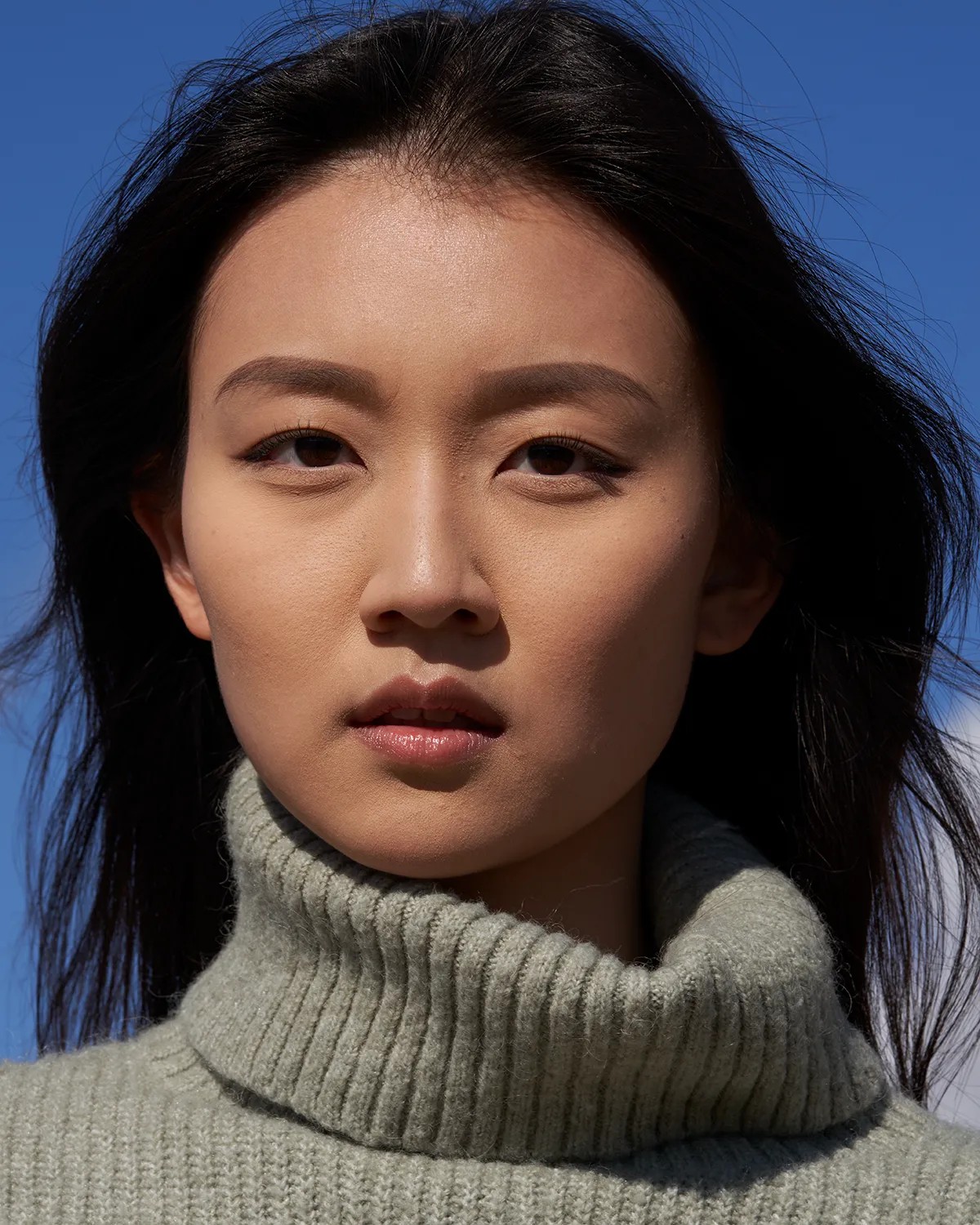 Actor headshot of a young woman with dark hair in a sage green turtleneck against a vivid blue sky — Headshots by Guffy, San Diego
