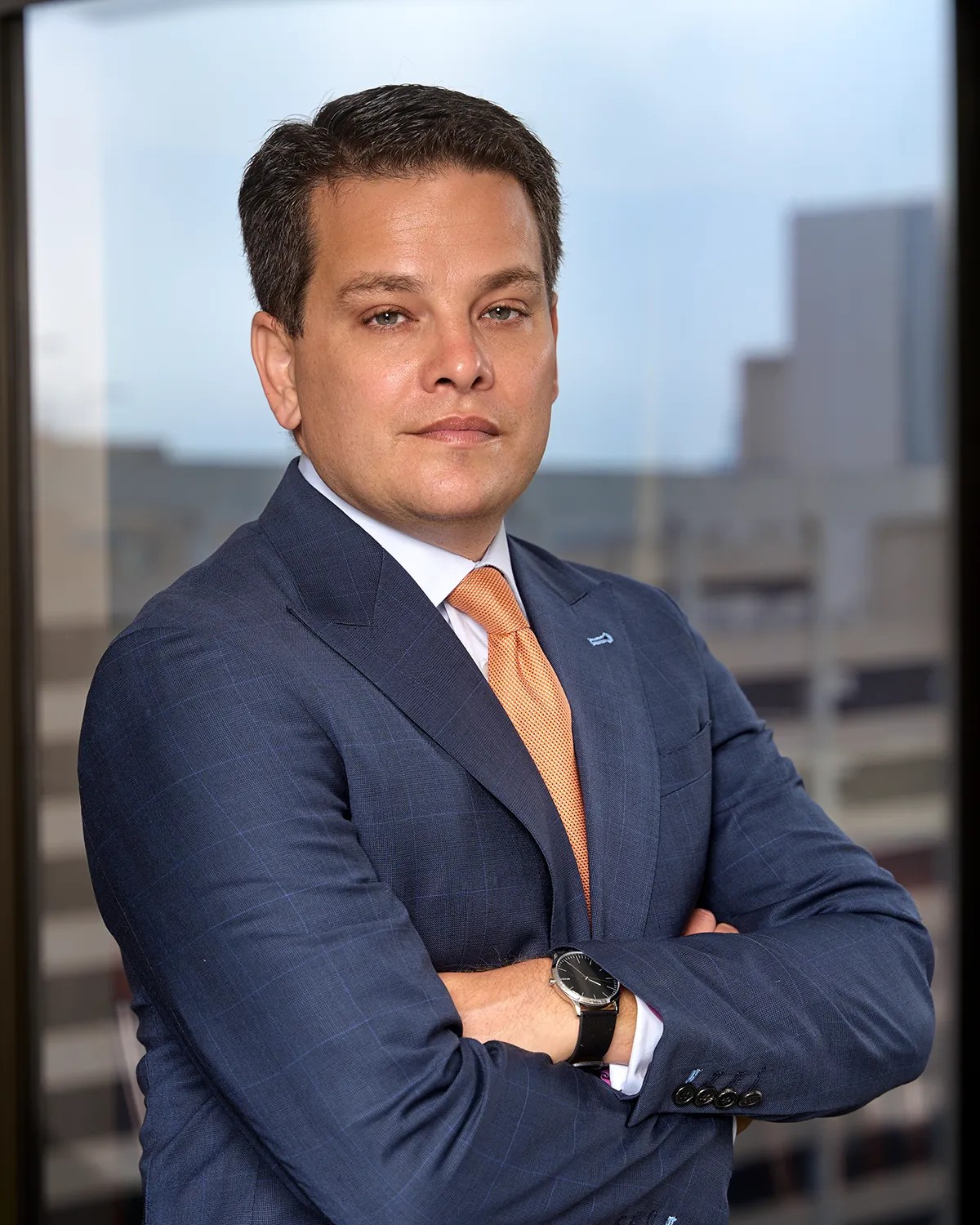 Executive headshot of a man in a navy plaid suit with arms crossed, photographed against a high-rise city window backdrop — Headshots by Guffy, San Diego