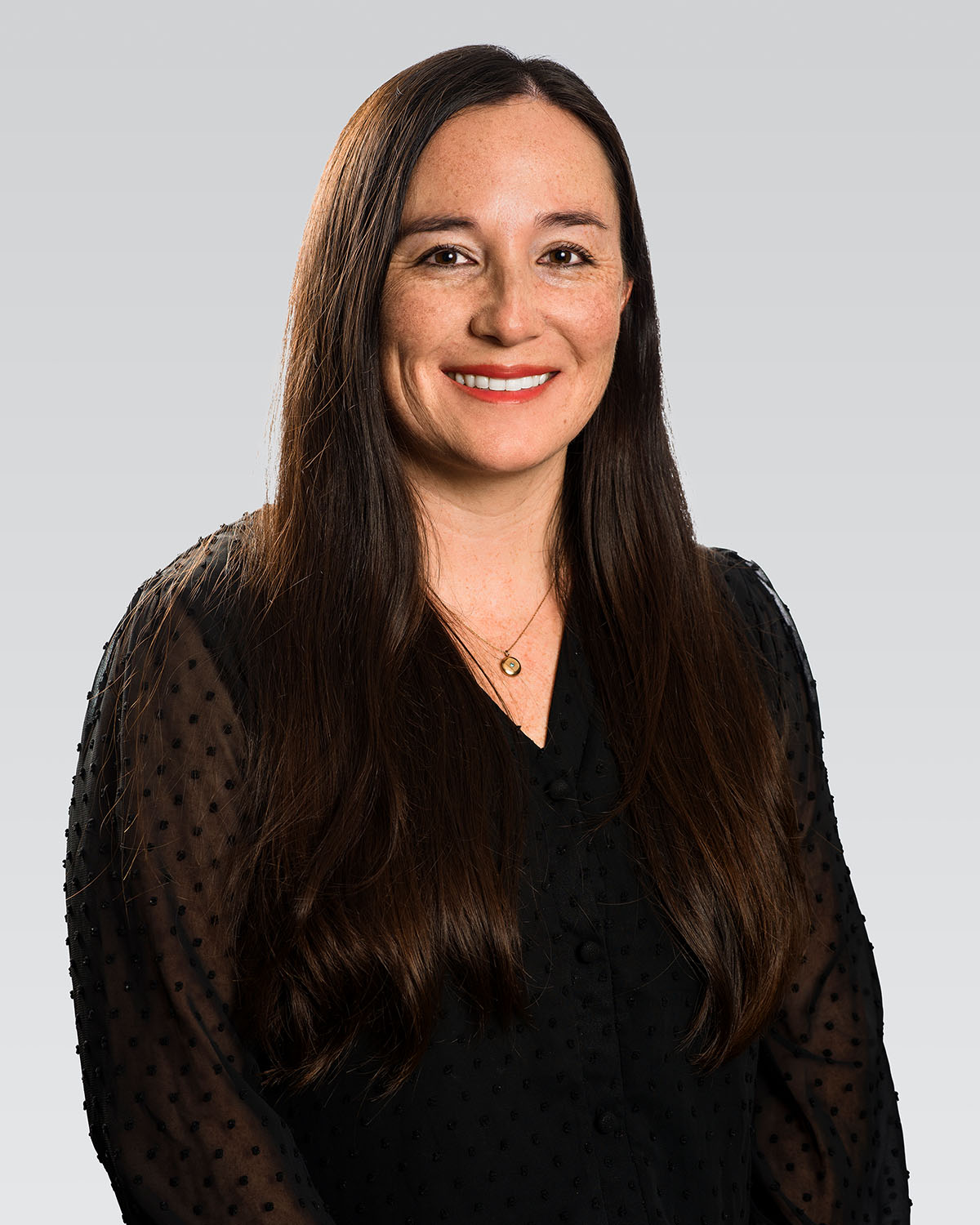 Professional headshot of a woman with long dark hair and red lip in a black top against a gray gradient background — Headshots by Guffy, San Diego