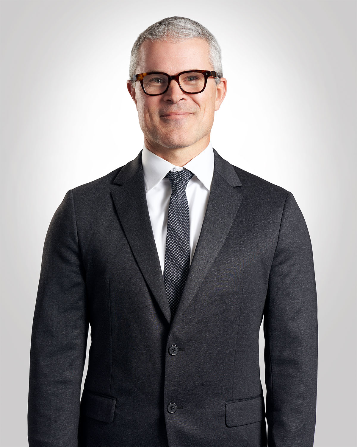 Executive headshot of a man in a navy suit with glasses against a gray gradient background — Headshots by Guffy, San Diego