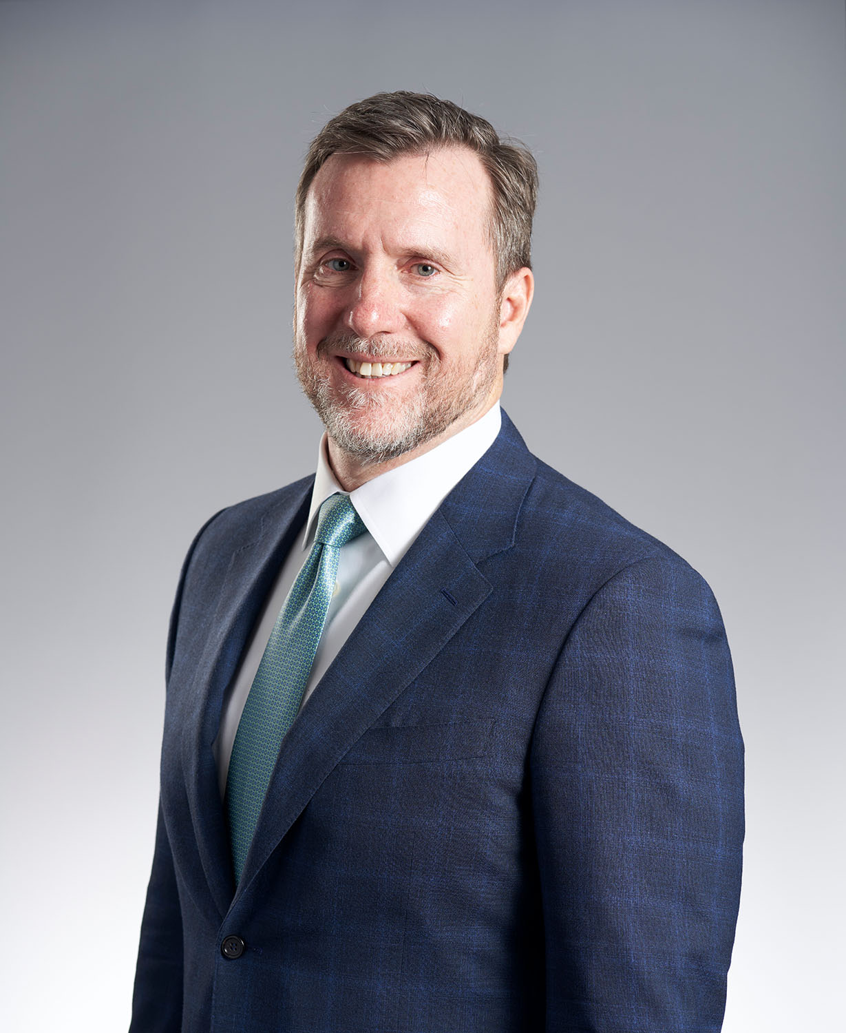Executive headshot of a man in a navy suit with a teal tie against a gray gradient background — Headshots by Guffy, San Diego