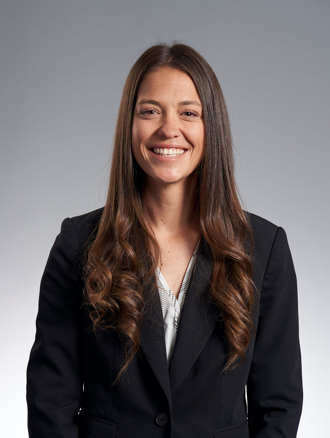 Professional headshot of a young woman with natural curly hair in a black blazer against a gray gradient background — Headshots by Guffy, San Diego